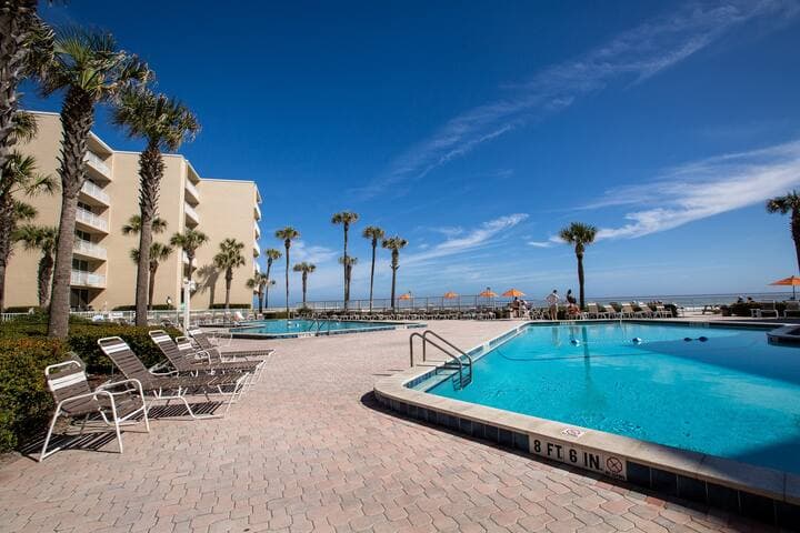 Large pool area with two pools and lots of chairs