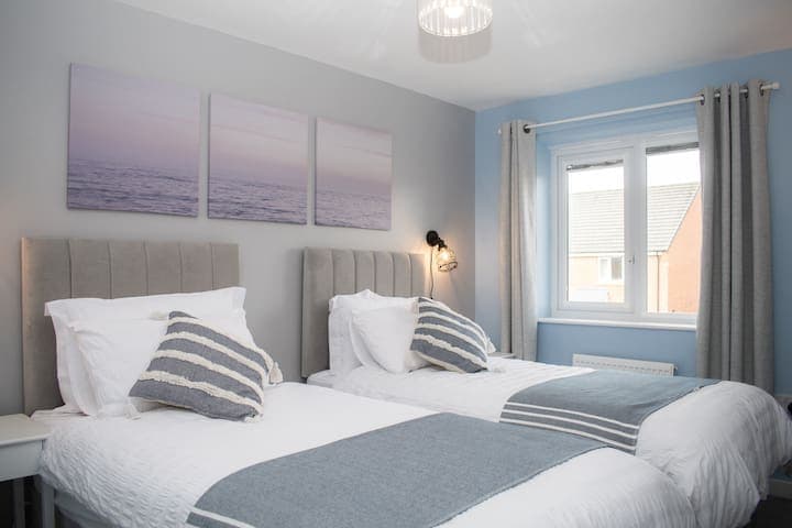 Twin bedroom with two single beds with individual bedside units, 4-way power adaptors with USB chargers and clothes storage with wooden hangers and drawers. A shelf contains a selection of mini board games.