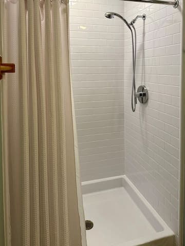 White subway tiled shower has a low entry and removable shower head