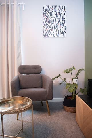 Living room with large comfortable L shaped sofa, additional chair, 65" Smart TV, football/foosball table and small table with stools.