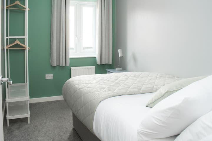 Double bed containing a bedside unit with lamp, 4-way power adaptor and USB charger, plus clothes storage with wooden hangers and blackout curtains.