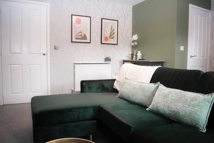 Living room with large comfortable L shaped sofa, additional chair, 65" Smart TV, football/foosball table and small table with stools.