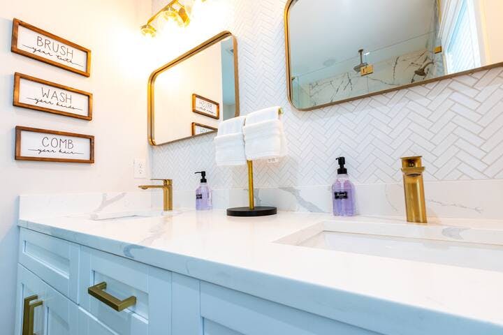 Bathroom 1: Indulge in luxury in the master bath suite featuring dual sinks with marble counters & elegant gold designer accents. Ample counter space, along with convenience of soft towels & provided hair/body/soap products, ensuring a pampered stay