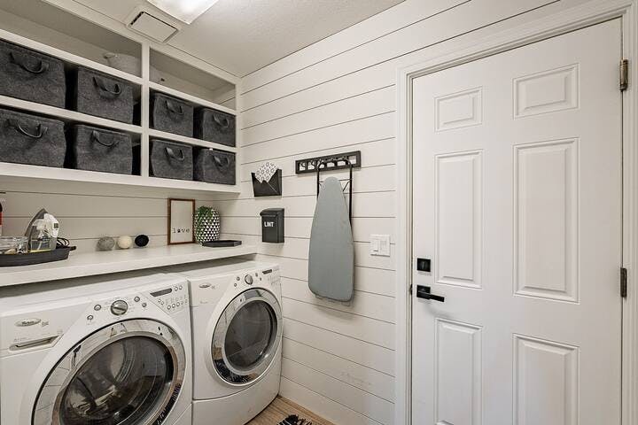 Completely furnished laundry area, featuring an iron and ironing board, detergent, and wool dryer balls