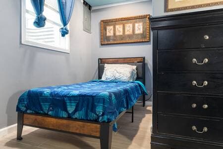 Twin Bedroom Retreat | Egress Window & Bed New egress window with blinds and navy curtains. Modern art above the twin bed with memory foam mattress. Charger and outlet built into the headboard. Second light switch on left. Black dresser on the right.