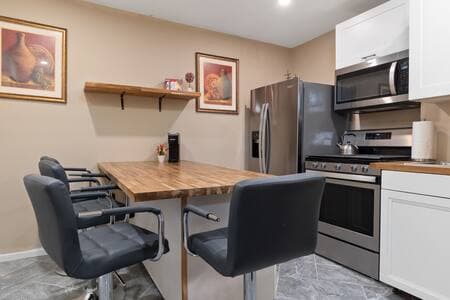 Kitchen Island | Barstools + Appliances Four new counter-height barstools around the island with matching butcher block countertop. Paintings hang on either side. Whirlpool gas stove and microwave. Fridge supplies filtered water and ice.