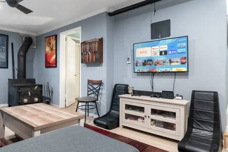 Living Room | Projector + Screen | Fireplace + Soundbar Pull down the 80" screen and turn on the projector for a cozy movie night. Soundbar adds rich audio. Bookshelf nearby. Door leads to Bedroom 1. Wood stove adds warmth.